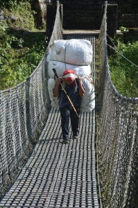 Ein Träger geht vollbeladen über eine Hängebrücke